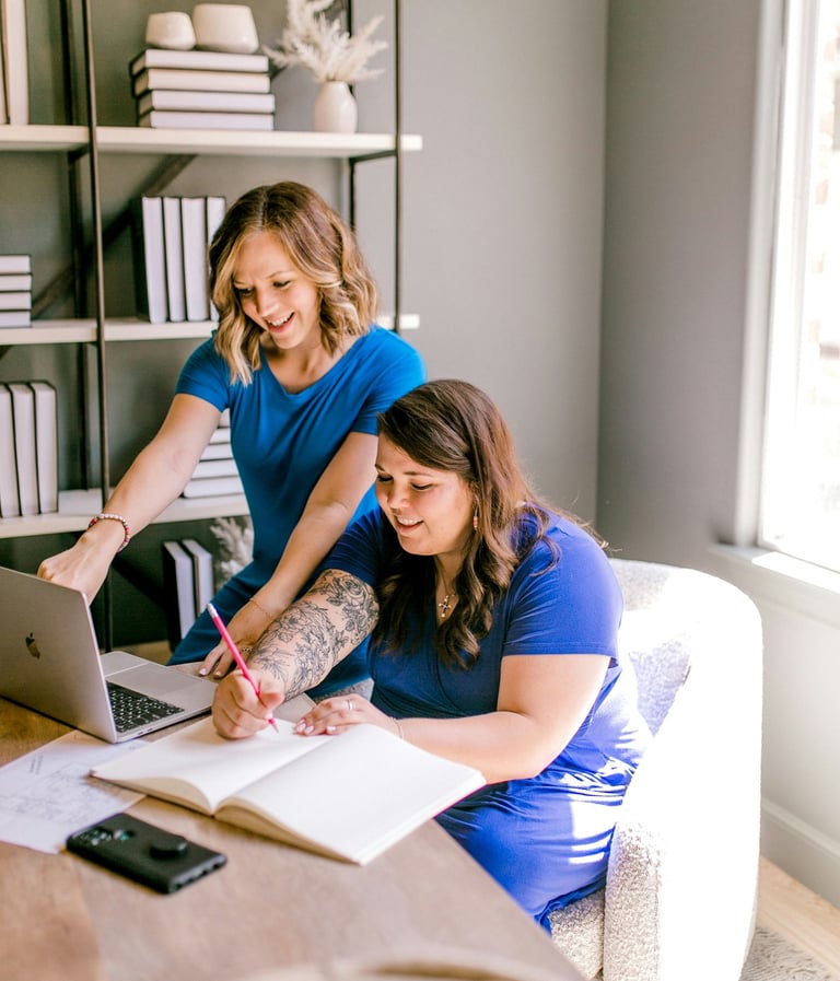 Two business women collaborating in a modern office with a laptop and notebook.