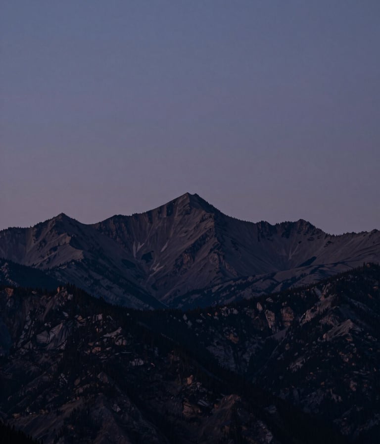 A cinematic wide shot of a North American mountain range at twilight. The sky is a muted indigo, and the silhouettes of the peaks are deep charcoal. The lighting is soft and professional, evoking quiet confidence.