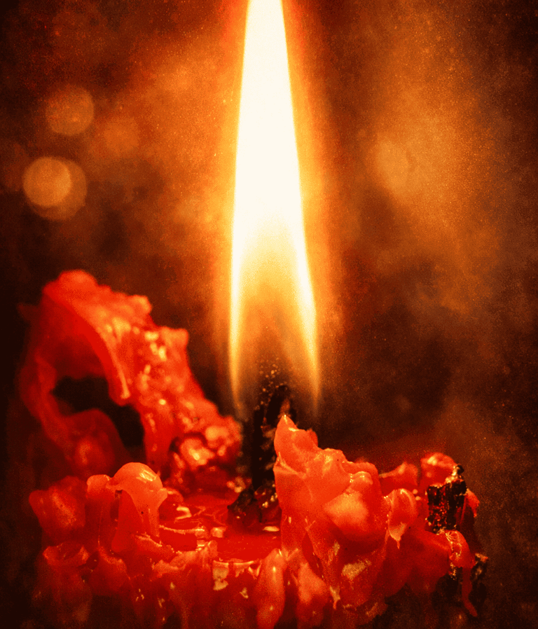 Una sola llama de vela roja encendida, con cera derritiéndose y un fondo de bokeh luminoso.