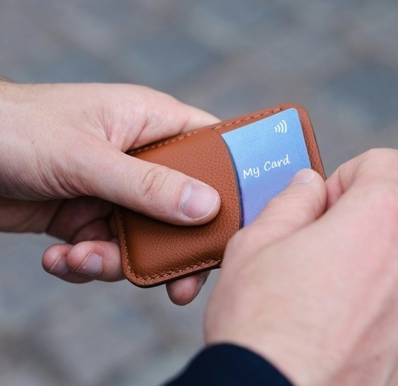 2 hands pulling a digital business card out of a stylish leather card holder on a blurry grey cloud background