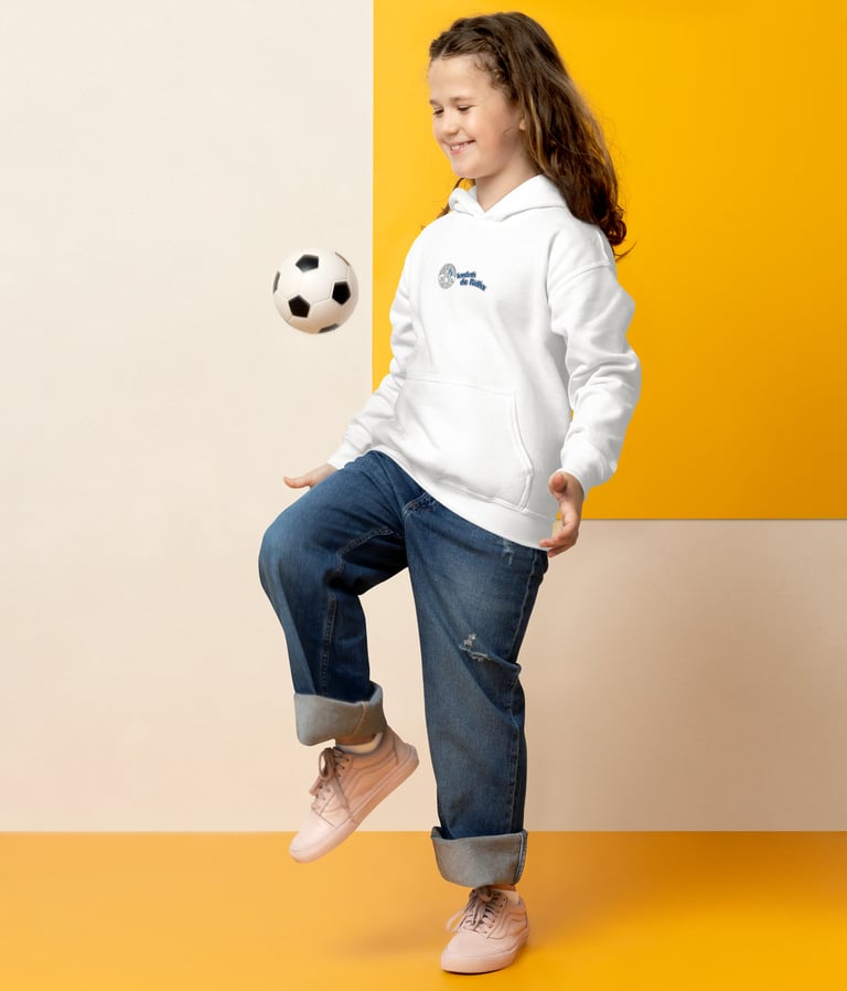 Young girl in a white hoodie and jeans balancing a soccer ball on her knee.