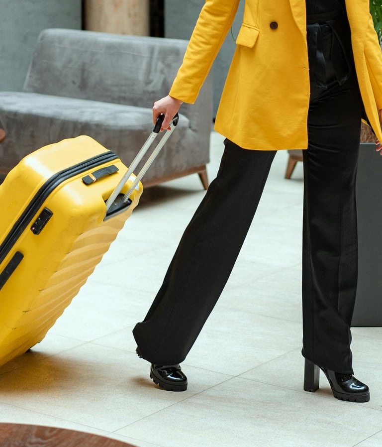A person in a yellow blazer pulling a matching yellow hardshell suitcase through a modern hotel lobby.