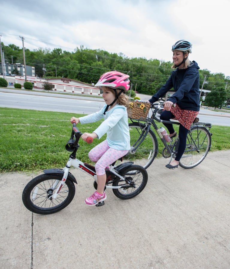 A mother and daughter riding bikes together on a sidewalk