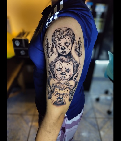 Tatuaje de realismo en negro y gris de tres querubines con rostros de payaso.