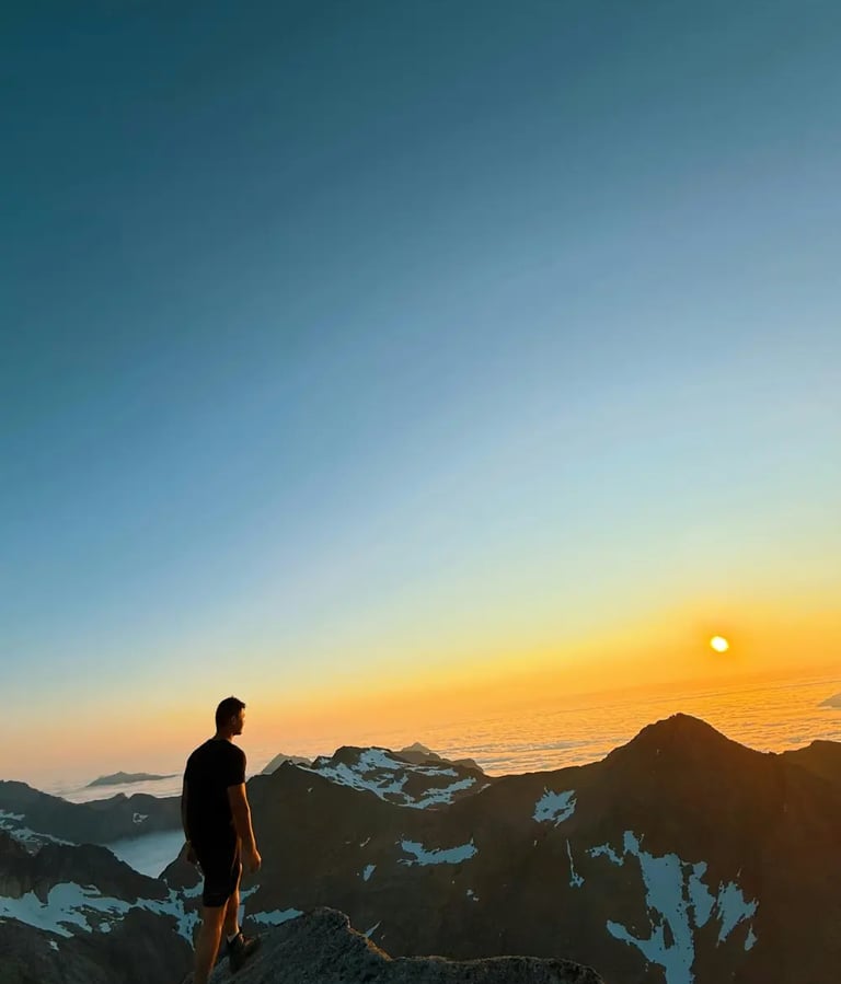 a man standing on a mountain top with a sunset in the background