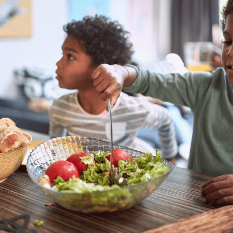 two children eating a salad in a bowl