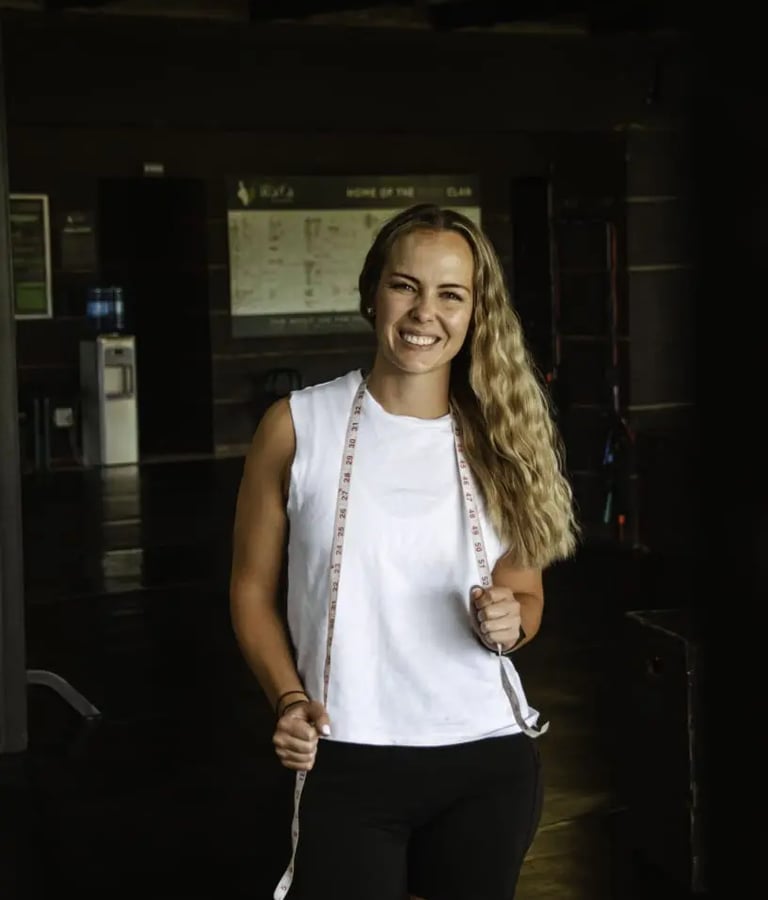 blond woman standing with white top and black exercise pants holding measurement band around her in hands
