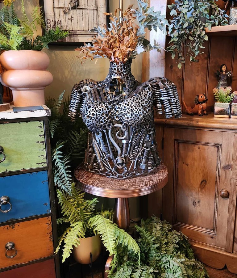 Steampunk female torso sculpture made of metal nuts, bolts and tools displayed in a rustic room.