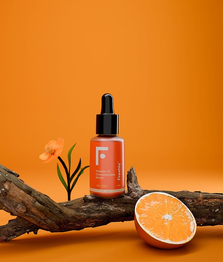 Bote de vitamina c de la marca Freshly, encima de un tronco con una flor al lado y un trozo de naranja.