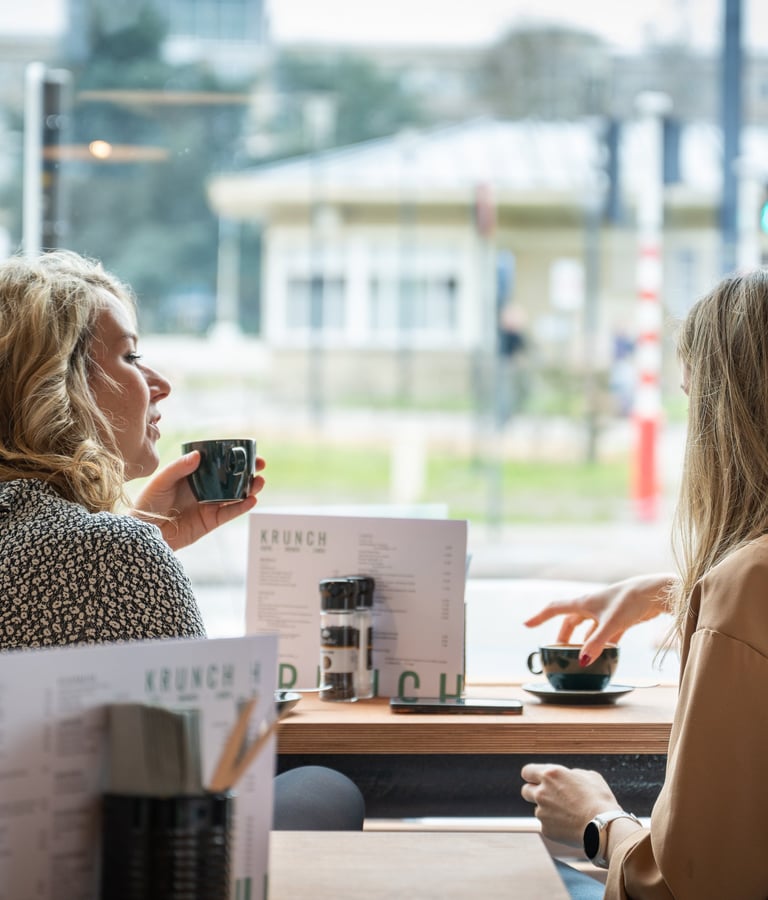 Twee bezoekers genieten van een koffie aan het raam bij Krunch Gent