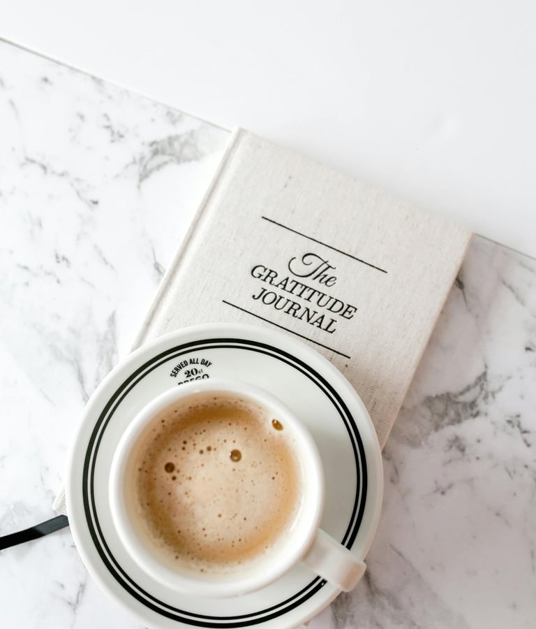 a frothy cup of coffee and a gratitude journal on a marble table