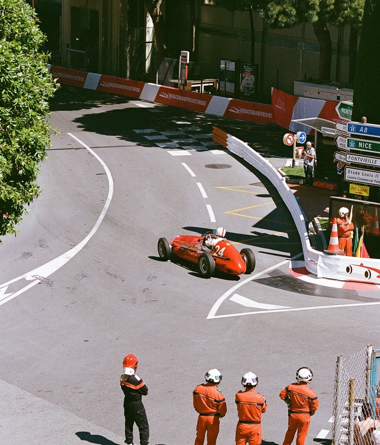 a group of race marshals watching a red race car go through a corner