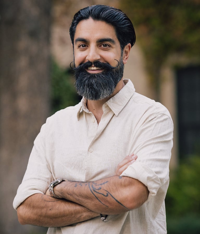 Eamon Moghimi smiling with arms crossed in a light shirt standing outdoors in a calm natural setting