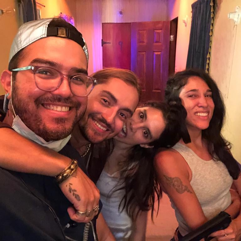 A group of four smiling friends posing for a playful selfie together indoors.