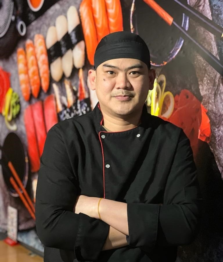 a chef in a black uniform and a black hat