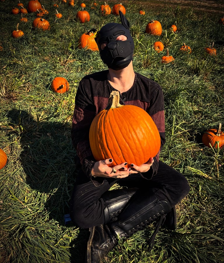 Man poses in a pumpkin patch wearing a pup mask.