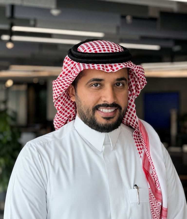 Smiling Saudi businessman wearing a traditional thobe and red shemagh in a modern office.