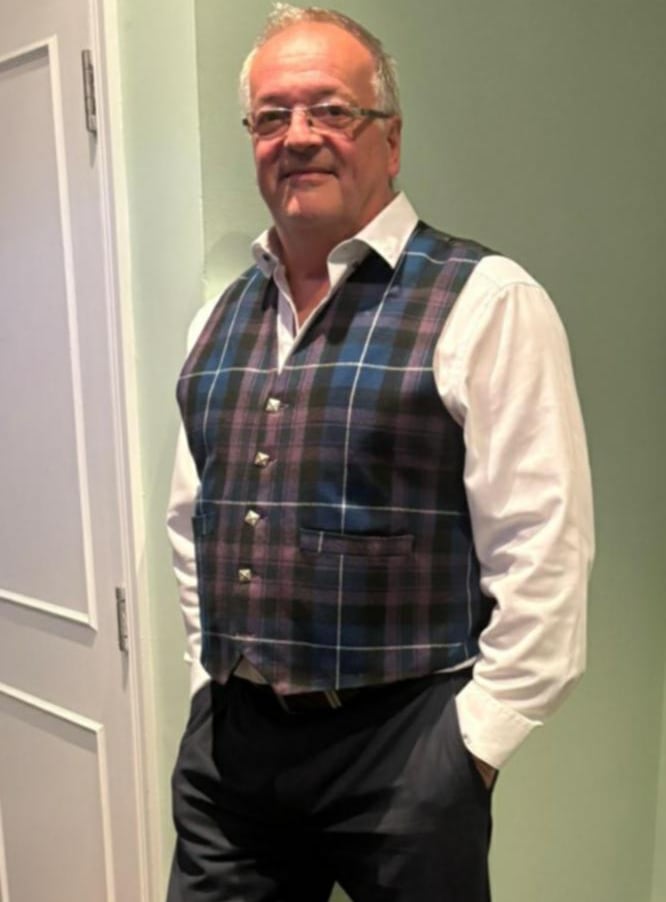 A man wearing a blue and purple tartan waistcoat over a white dress shirt.