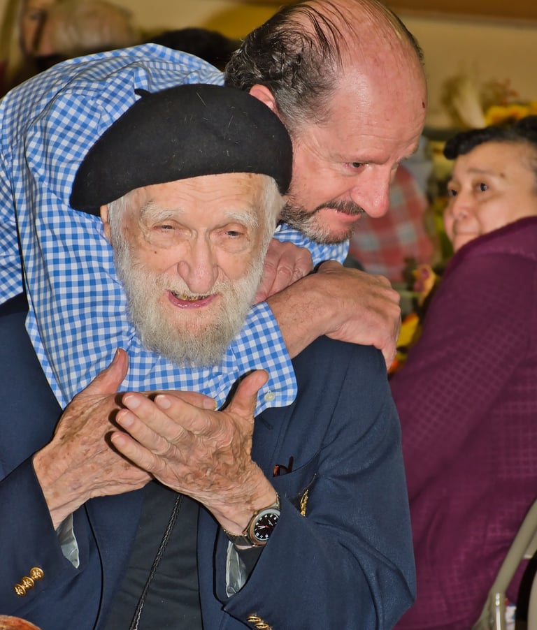 a man in a blue jacket is holding an old man's shoulder 