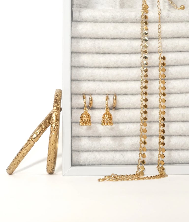 Gold jewellery collection arranged on a white display with earrings and layered anklets