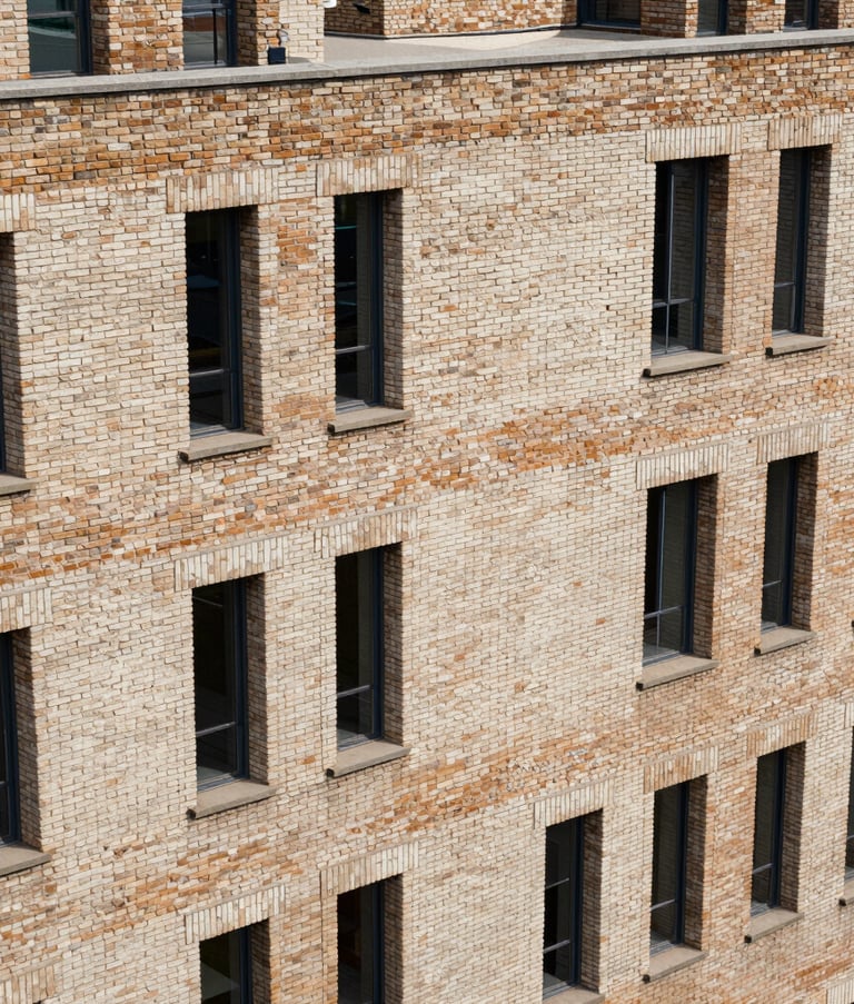 A high-angle shot of a European modern architectural building constructed with multi-toned medium tan and off-white clay bricks, showcasing exceptional craftsmanship and a robust industrial design.
