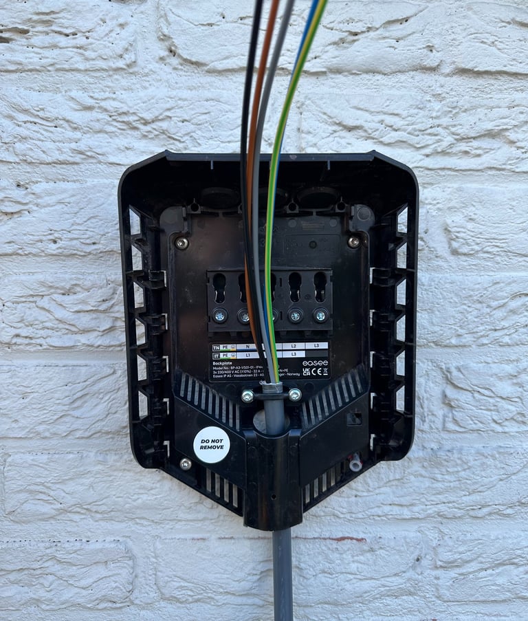 Internal wiring of an Easee electric vehicle charging station mounted on a white brick wall.