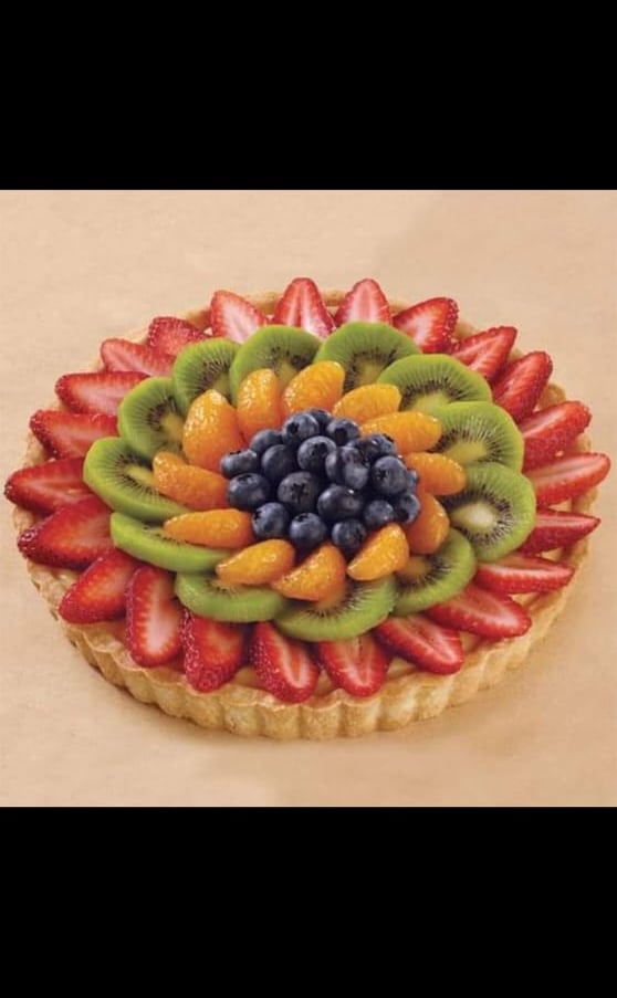 Tarta de frutas frescas cubierta con círculos concéntricos de fresas, kiwi, naranjas y arándanos.