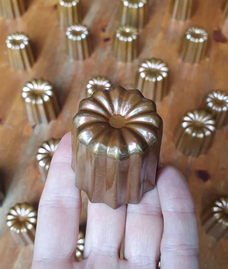 Un moule à cannelé en cuivre tenu dans une main