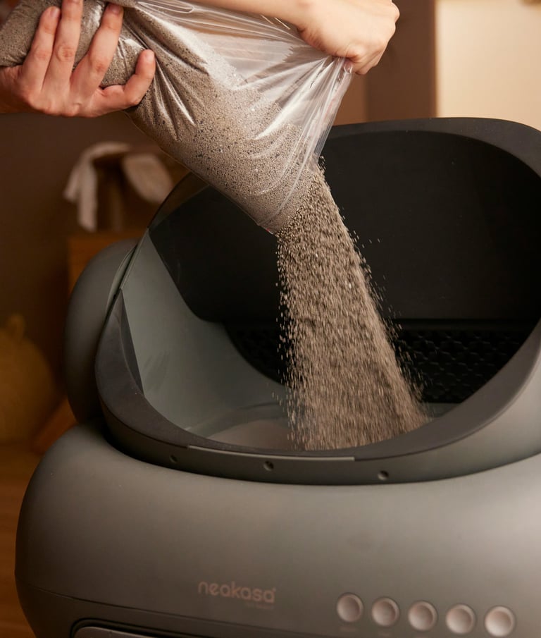 A person pours fresh clumping litter from a bag into an automatic self-cleaning Neakasa cat litter box.