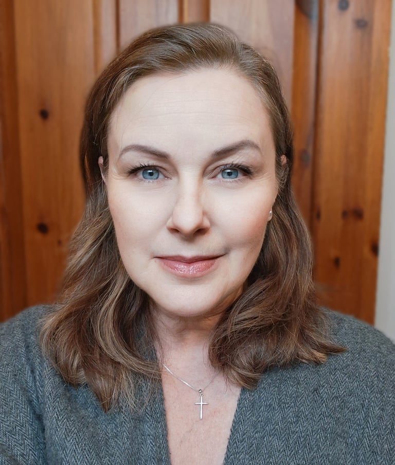 Professional headshot of a woman with blue eyes and brown hair wearing a silver cross necklace.
