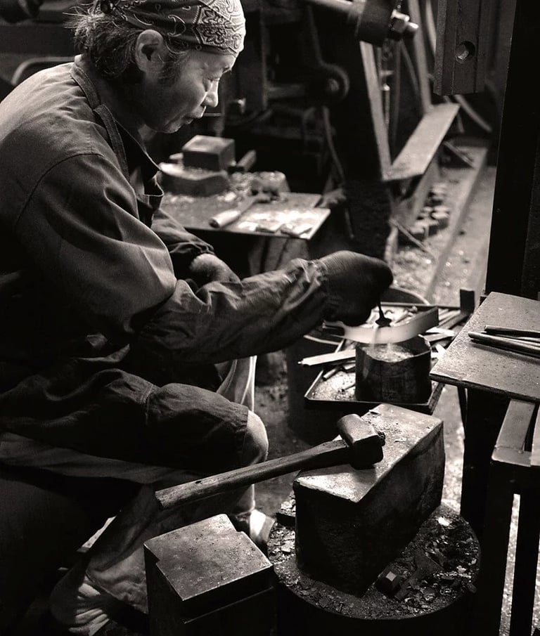 Historische Schwarzweißaufnahme eines japanischen Messerschmieds in einer traditionellen Schmiede in