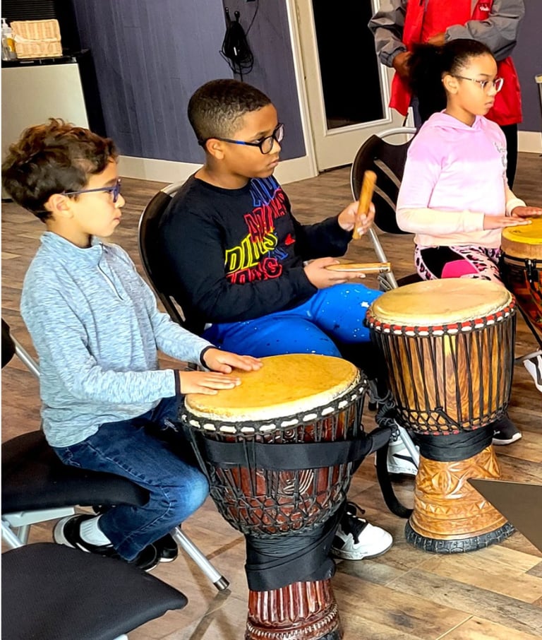 young children play djembe drums