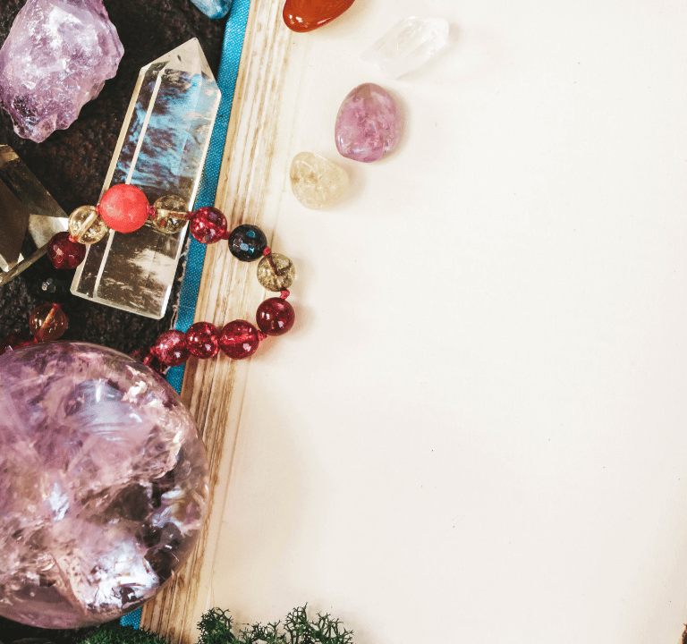 Healing crystals, amethyst sphere, and beaded bracelet arranged on an open blank vintage journal.