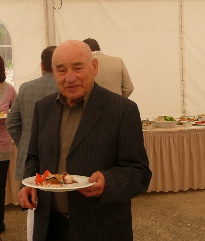 An elderly man in a pinstripe suit holding a plate of food at a catered buffet event.