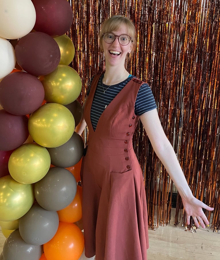 Natalie in a dress and glasses standing in front of a balloon arch