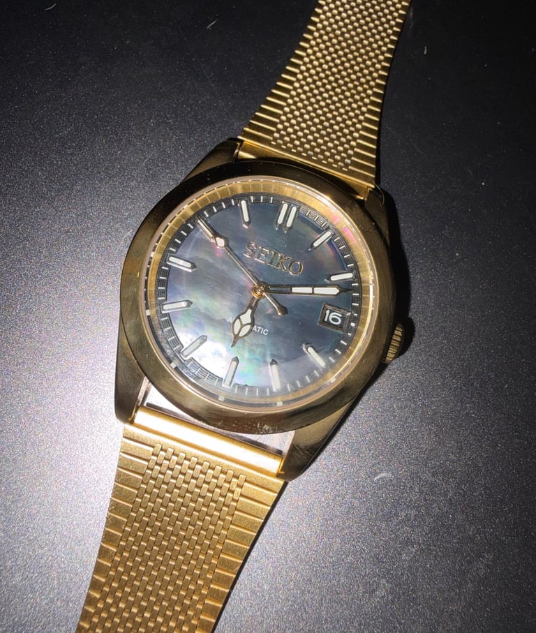 Gold Seiko automatic watch with a black mother of pearl dial and mesh bracelet strap.