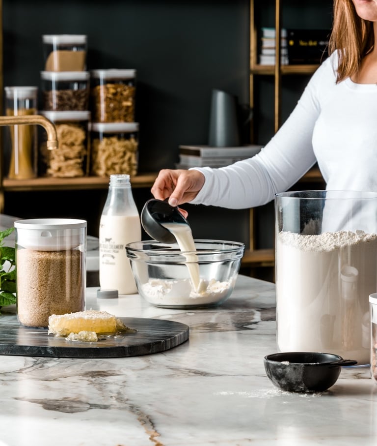 Food product photography - a woman in a white shirt pouring milk in a bowl of flour