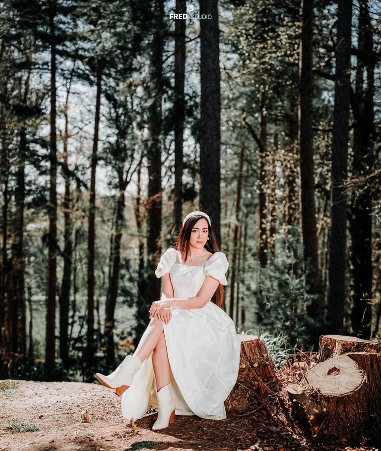 Bride sitting gracefully among tall forest trees in Surrey, photographed by Fred Art Studio.