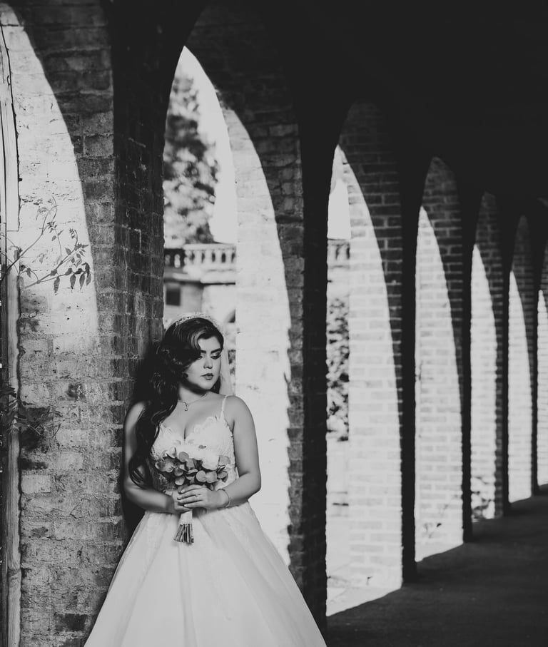 B&W portrait of a bride holding her bouquet under brick arches, photographed by Fred Art Studio.
