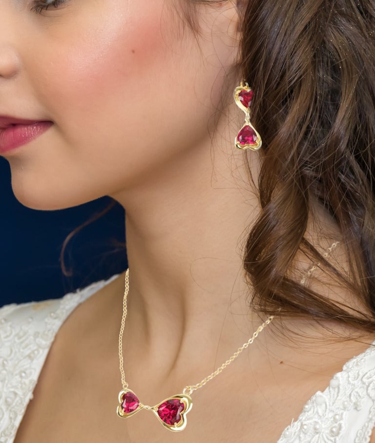 a woman wearing a gold eternal love knot necklace and earrings with a ruby heart
