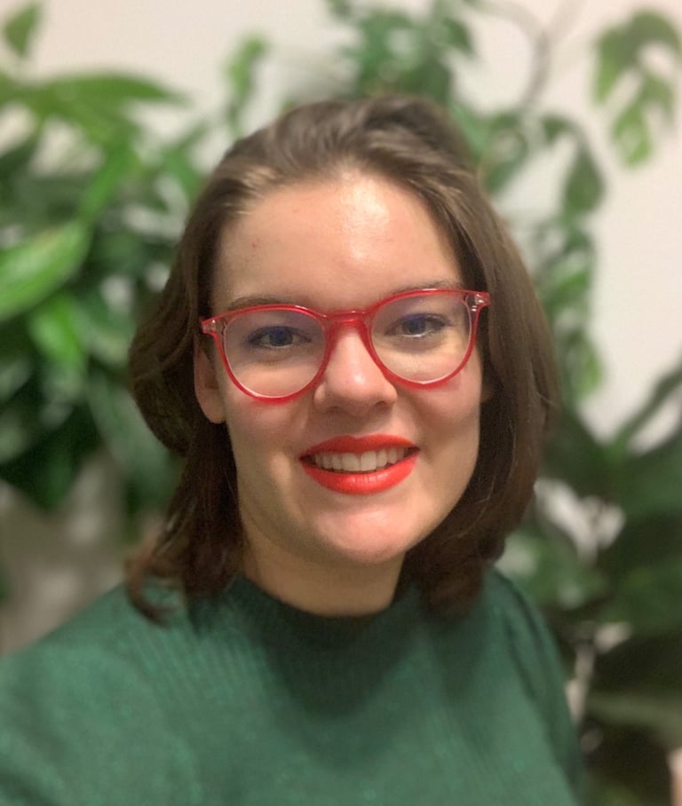 A portrait of a woman with shoulder-length brown hair, wearing red glasses and a green top, smiling