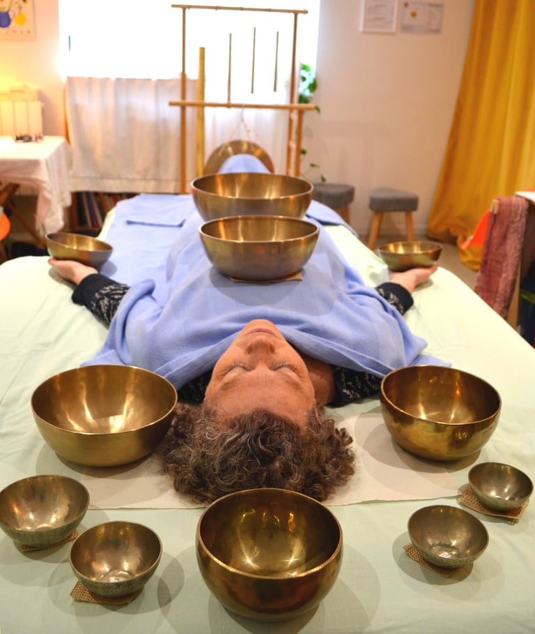 Une femme pendant une séance de sonothérapie entourée de bols chantants.
