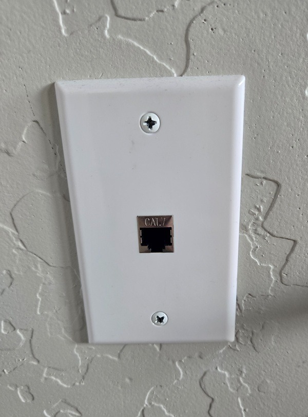 White Cat 7 ethernet wall plate with a single RJ45 network jack installed on a textured wall.