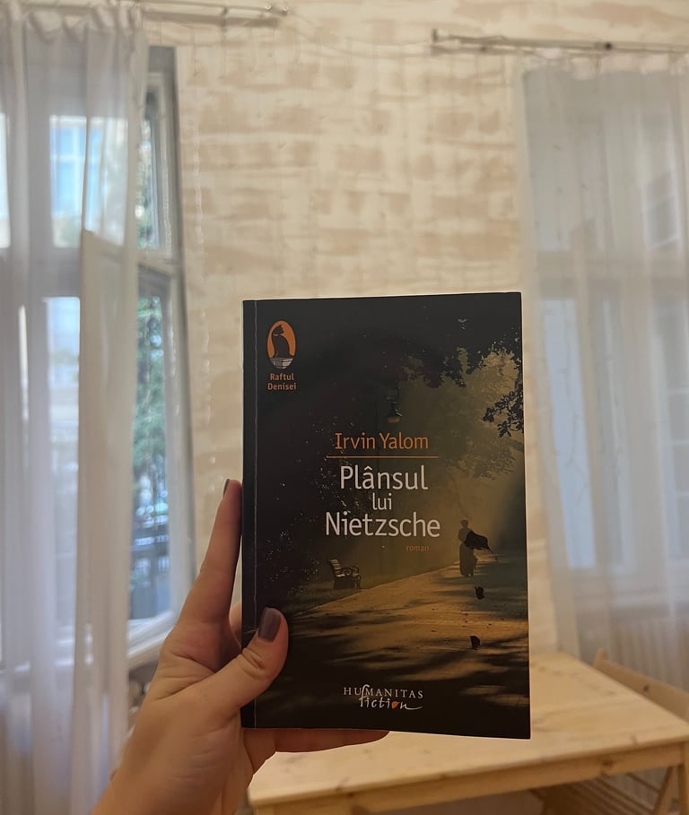 Mână ținând cartea 'Plansul lui Nietzsche' de Irvin Yalom pe un fundal de luminițe de basm.