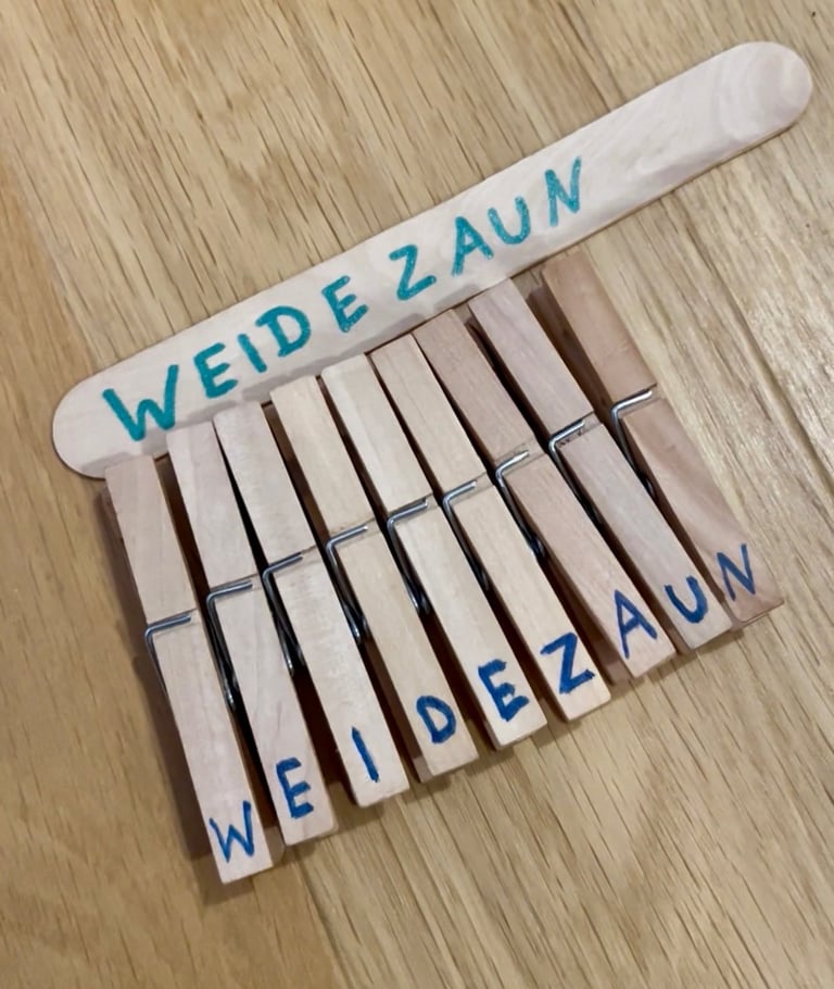 Wooden clothespins and craft stick featuring the word WEIDEZAUN in blue marker for a kids DIY project.