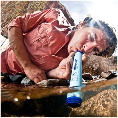 A hiker using a LifeStraw personal water filter to drink directly from a natural stream while outdoors.