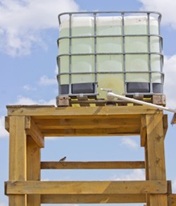 White IBC tote water tank on a tall wooden platform for gravity-fed irrigation.