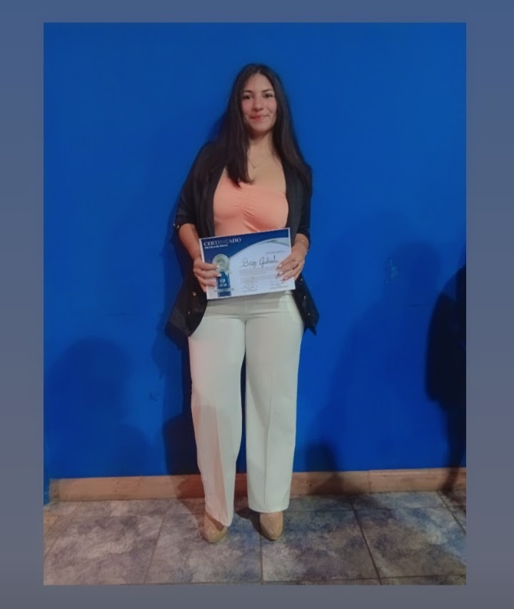 Professional woman holding a certificate of achievement in front of a blue wall background.