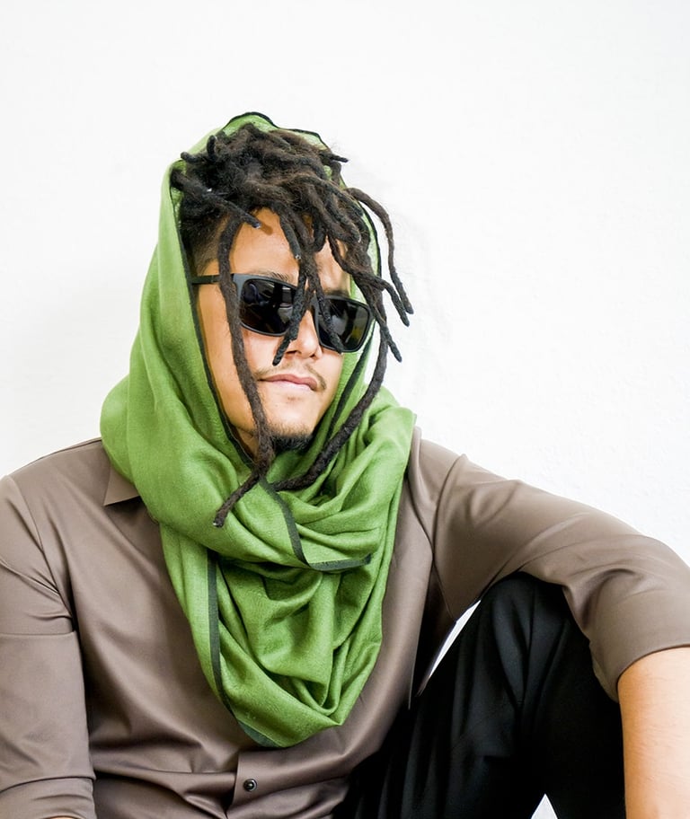 Man with dreadlocks wearing sunglasses and green pashmina scarf, styled with brown shirt and watch.