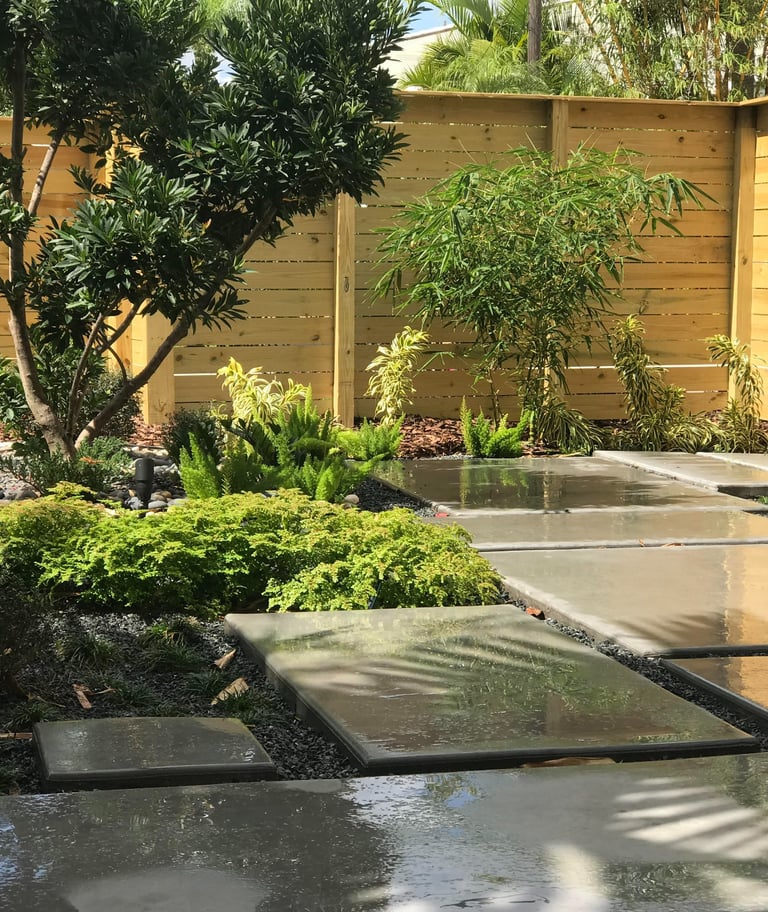 Modern garden landscape with concrete paver walkway, lush green plants, and a horizontal wood fence.